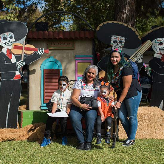 Group with Sugar Skull Face Paint Posing with Themed Backdrop at AltaMed Día de Muertos Picnic in Los Angeles